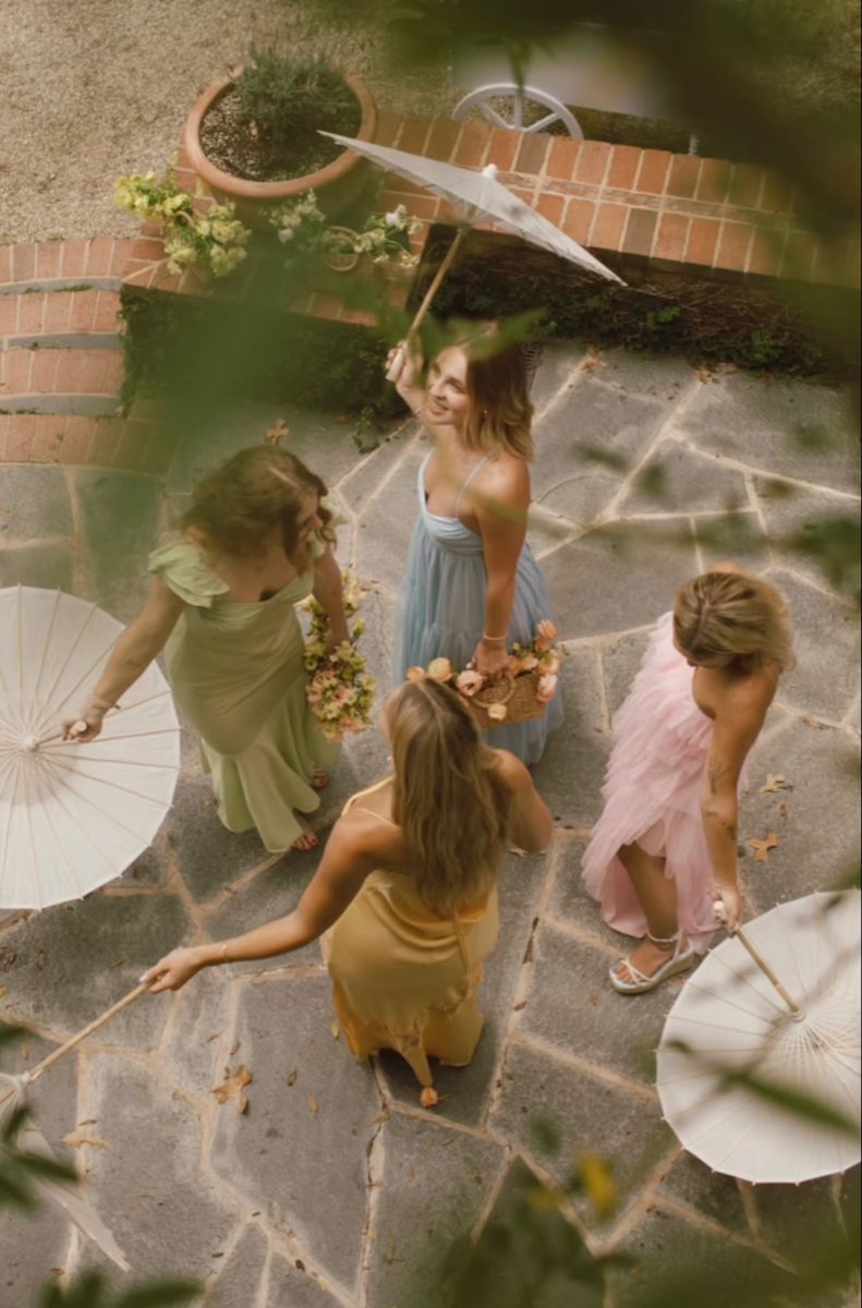 Overhead view of guests in pastel dresses holding paper parasols on stone courtyard